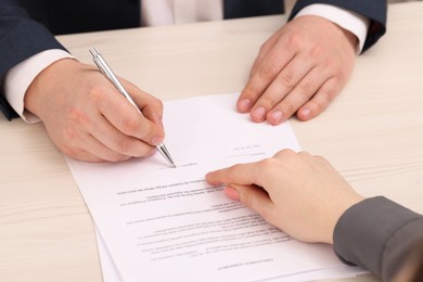 Photo of Woman pointing at document and man putting signature at wooden table, closeup