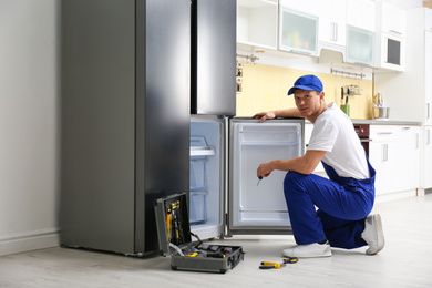 Male technician with screwdriver repairing refrigerator in kitchen