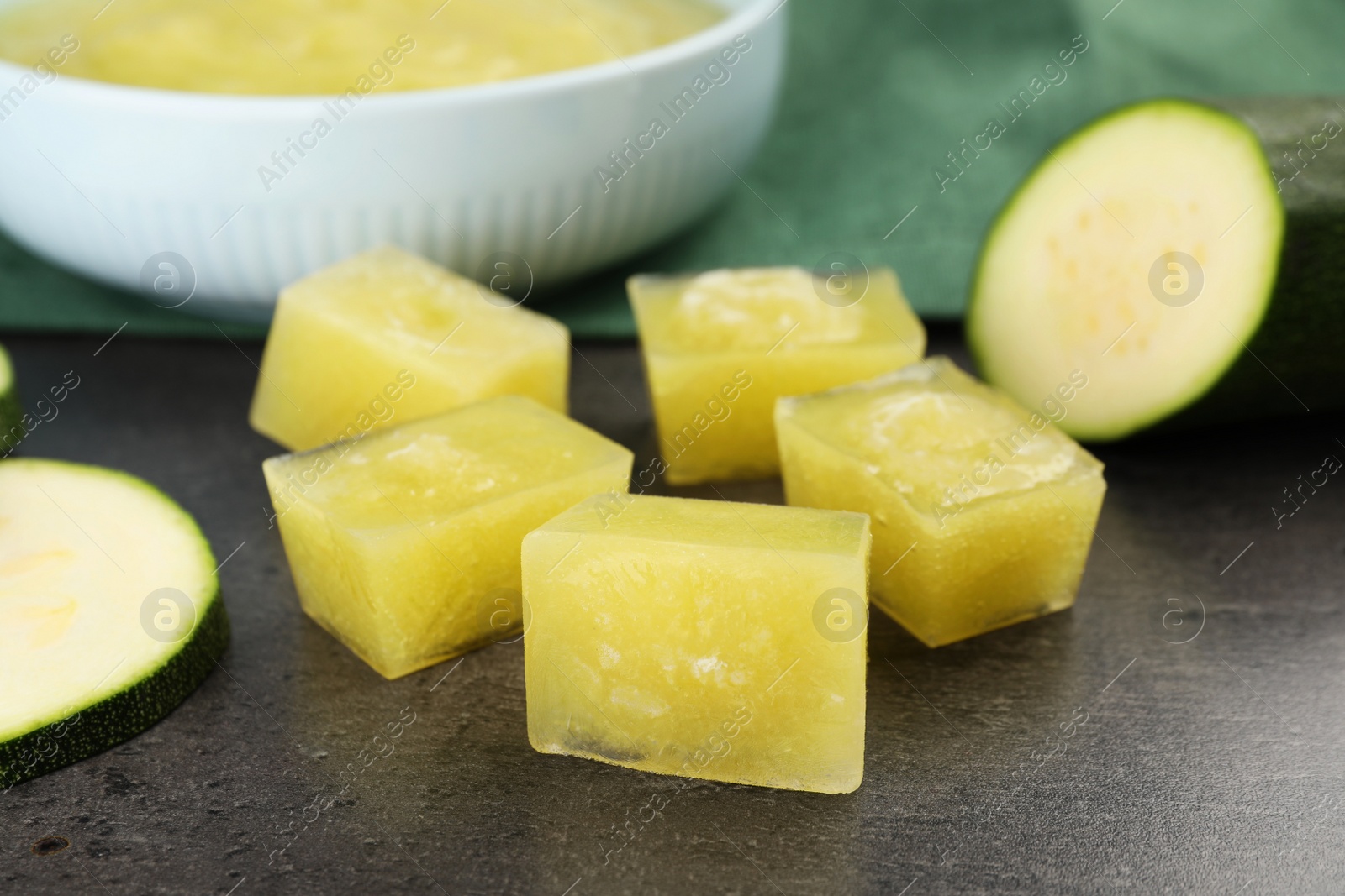 Photo of Frozen zucchini puree cubes and fresh zucchini on grey table, closeup