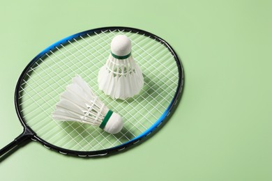 Feather badminton shuttlecocks and racket on green background, above view. Space for text