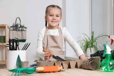 Little girl adding soil into peat pots at wooden table indoors. Growing vegetable seeds