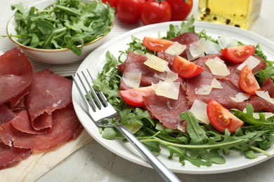 Photo of Delicious bresaola salad with parmesan cheese served on light grey textured table, closeup
