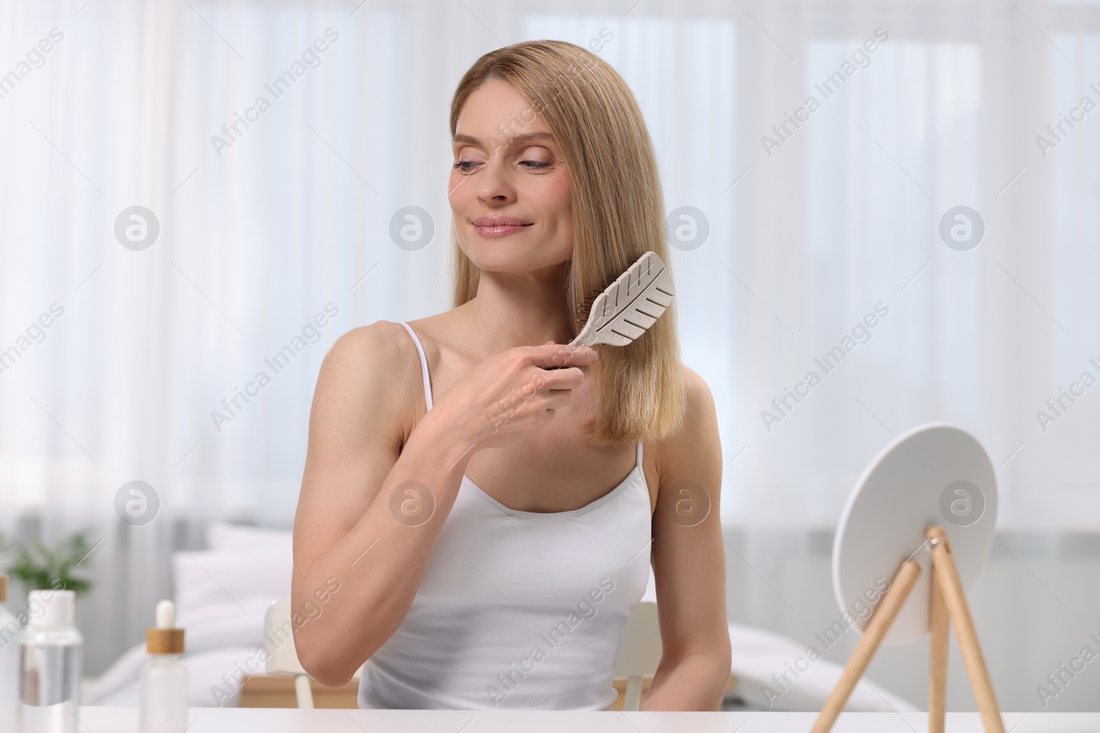 Photo of Beautiful woman brushing her hair in bedroom