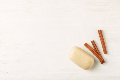 Flat lay composition with soap bar, cinnamon sticks and space for text on white wooden background