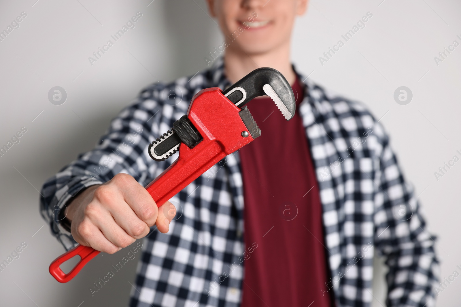 Photo of Handyman with pipe wrench against light background, focus on hand