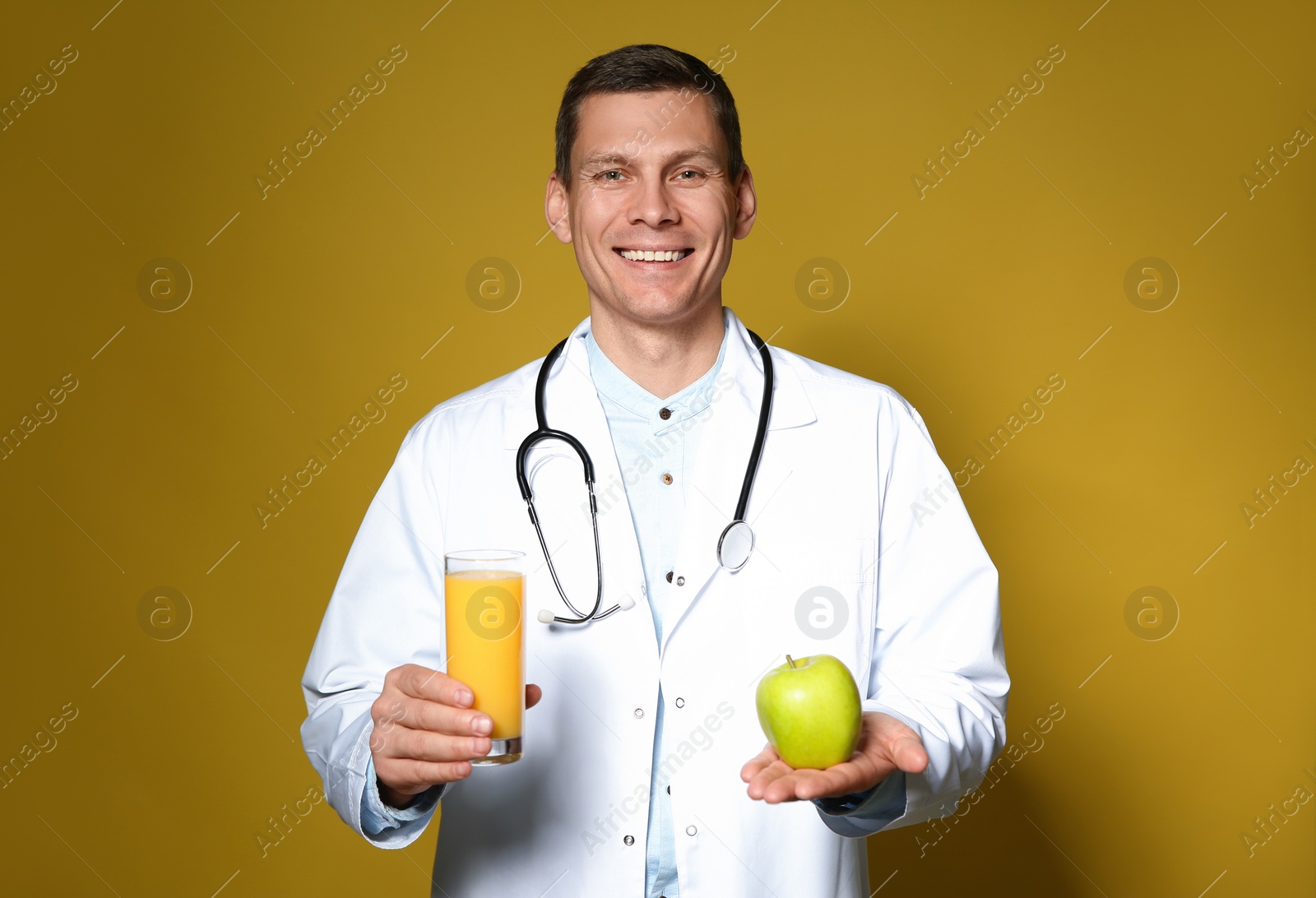 Photo of Nutritionist holding glass of juice and apple on yellow background
