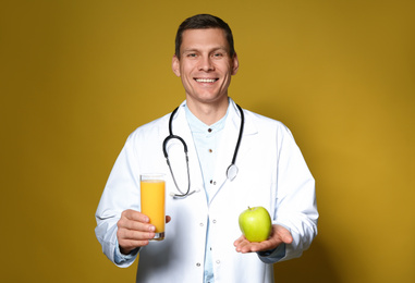 Photo of Nutritionist holding glass of juice and apple on yellow background