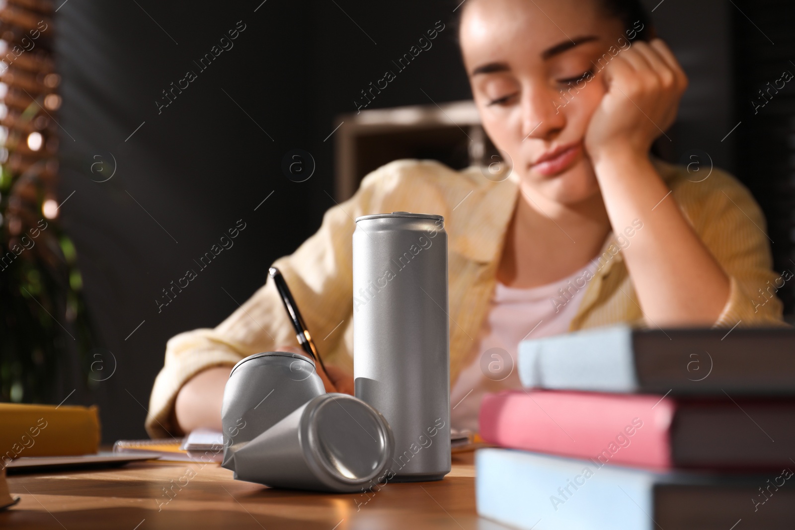 Photo of Tired young woman with energy drink studying at home, focus on cans