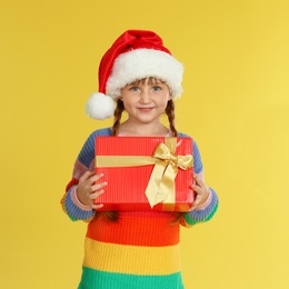 Photo of Cute little girl in Santa hat with Christmas gift on yellow background