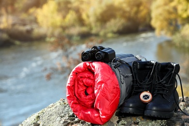 Photo of Set of camping equipment with sleeping bag on rock outdoors. Space for text