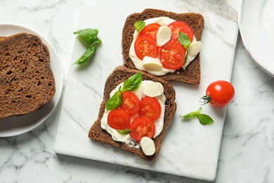 Photo of Toast bread with cherry tomatoes and mozzarella cheese on marble board, top view