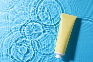 Tube with moisturizing cream in water on light blue background, top view. Space for text