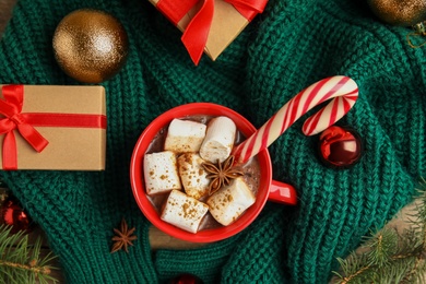 Photo of Cup of tasty cocoa with marshmallows, candy cane and Christmas decor on table, flat lay