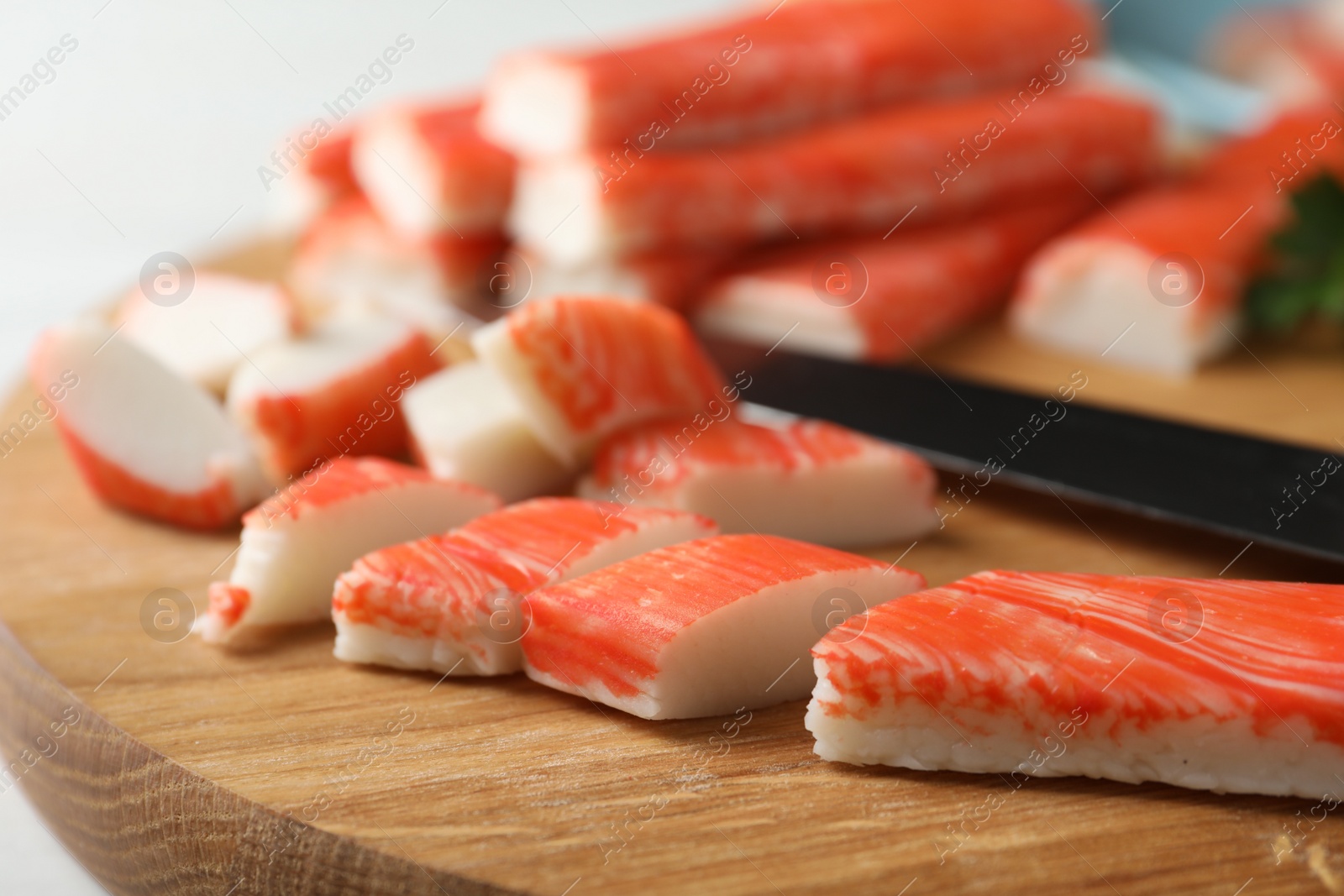 Photo of Sliced crab sticks and knife on wooden cutting board, closeup