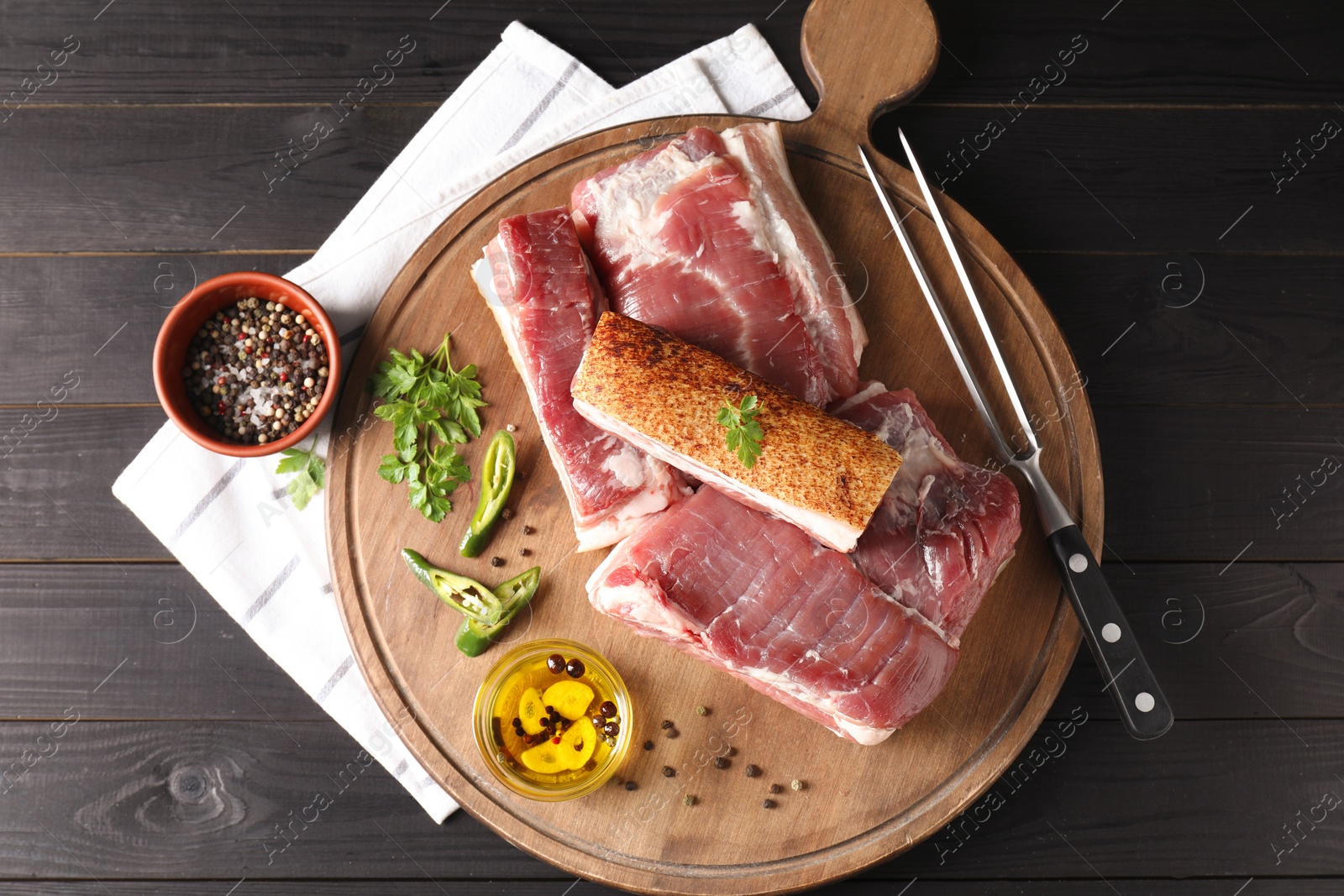 Photo of Pieces of raw pork belly, chili pepper, peppercorns, oil and parsley on black wooden table, top view