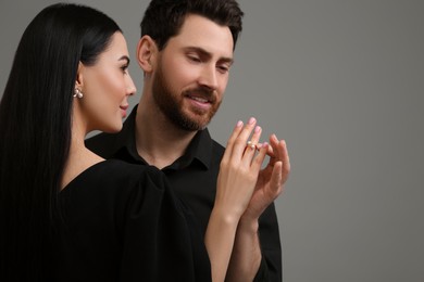 Photo of Man putting elegant ring on woman's finger against dark grey background