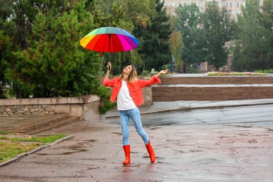 Happy young woman with bright umbrella under rain outdoors