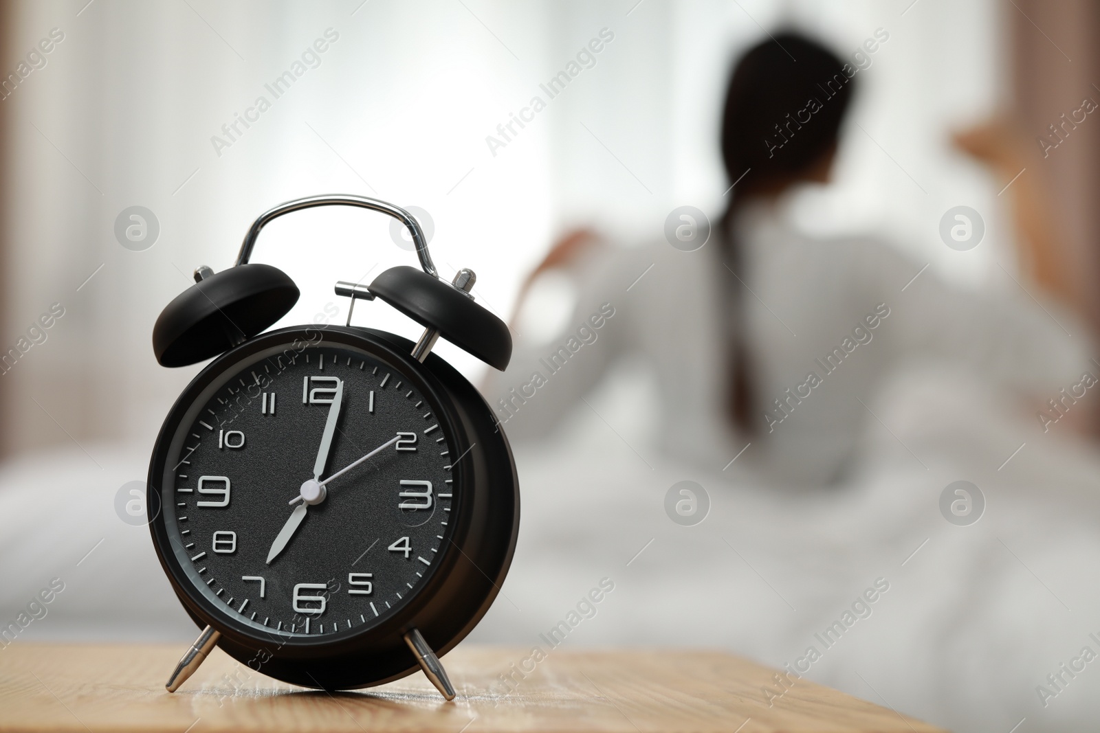 Photo of Woman stretching in bedroom, focus on alarm clock. Space for text