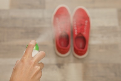 Woman spraying deodorant over pair of shoes at home, closeup. Space for text