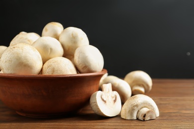 Bowl with fresh champignon mushrooms on wooden table, closeup. Space for text