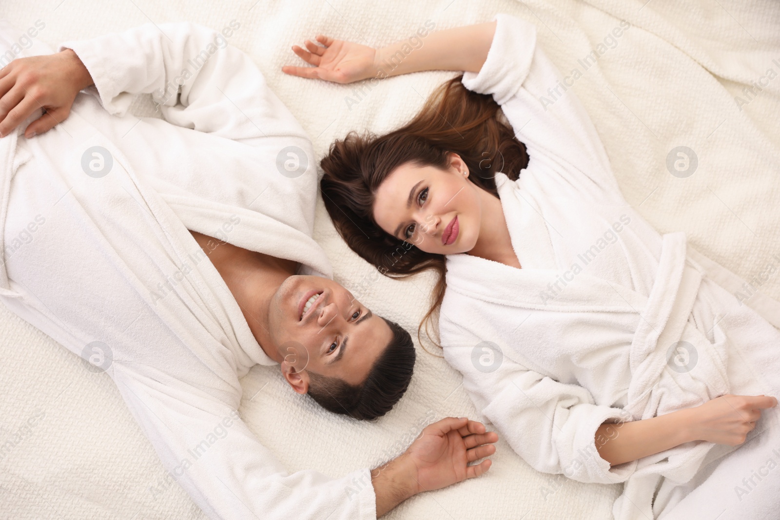 Photo of Happy couple in bathrobes lying on bed, top view