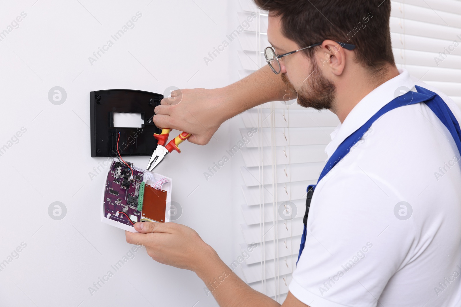 Photo of Technician installing home security alarm system on white wall indoors