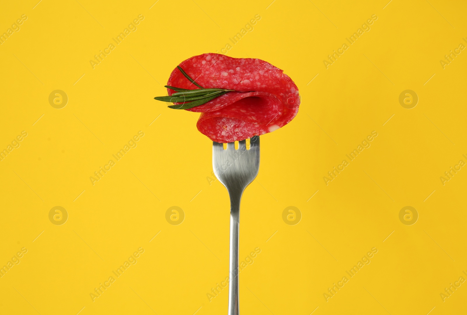 Photo of Fork with tasty slice of salami and rosemary on orange background