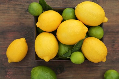 Many fresh lemons and limes with leaves on wooden table, flat lay