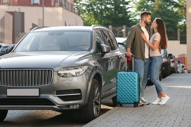 Photo of Long-distance relationship. Beautiful young couple with luggage hugging near car outdoors