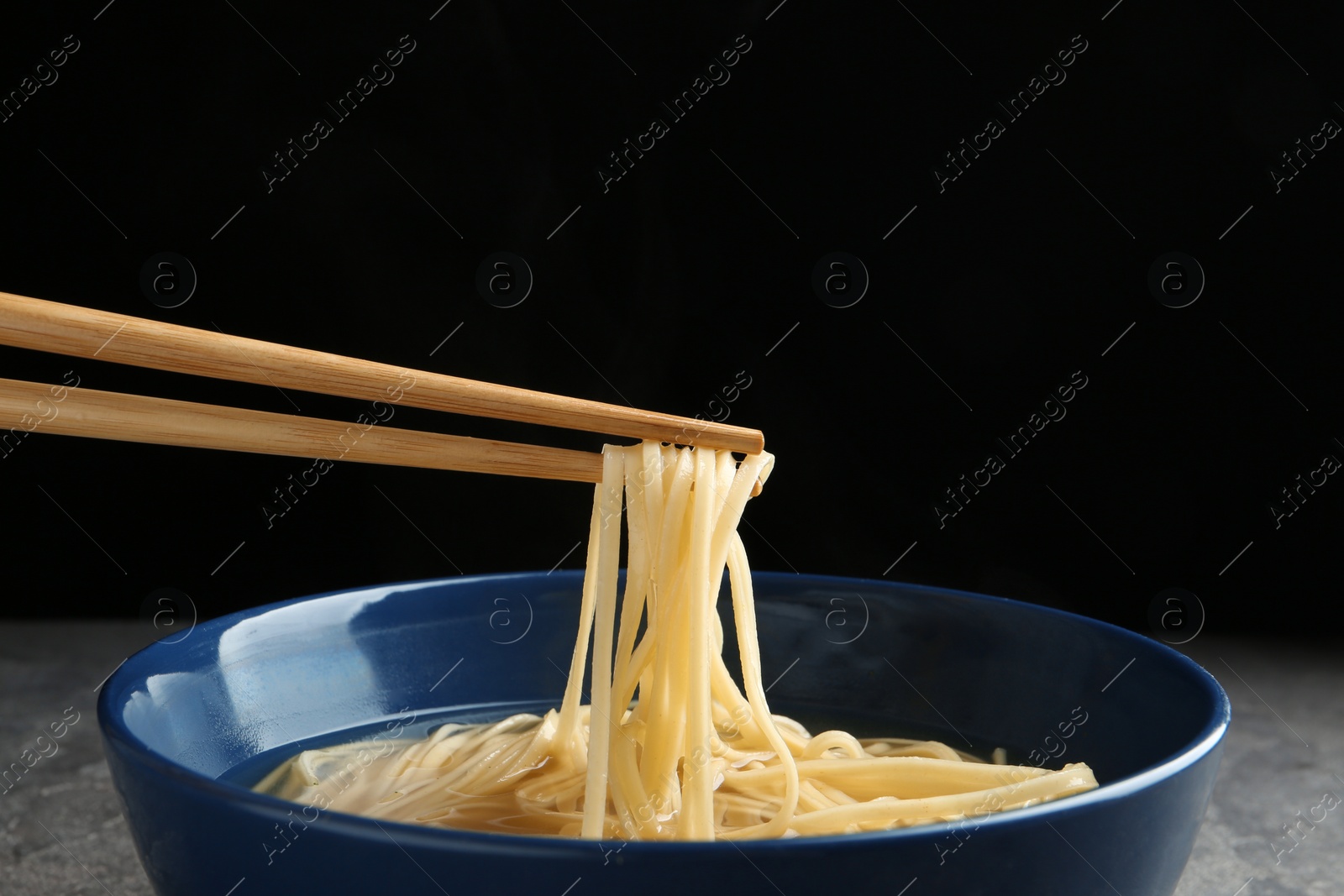 Photo of Eating noodle dish with chopsticks against black background