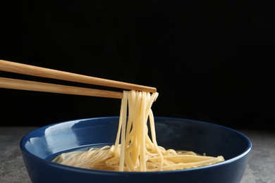 Eating noodle dish with chopsticks against black background