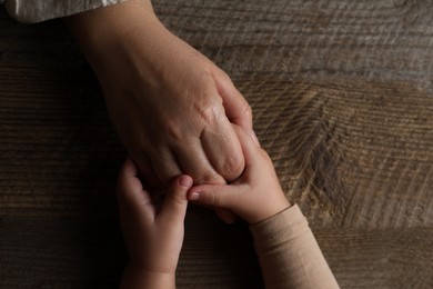 Photo of Woman holding hands with her granddaughter at wooden table, top view. Space for text