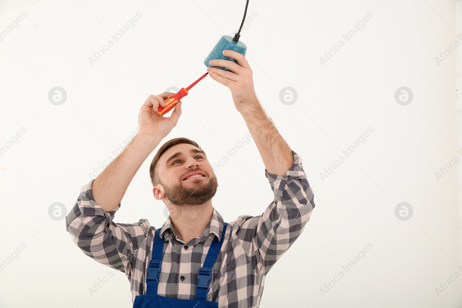 Photo of Electrician with screwdriver repairing ceiling lamp against white background