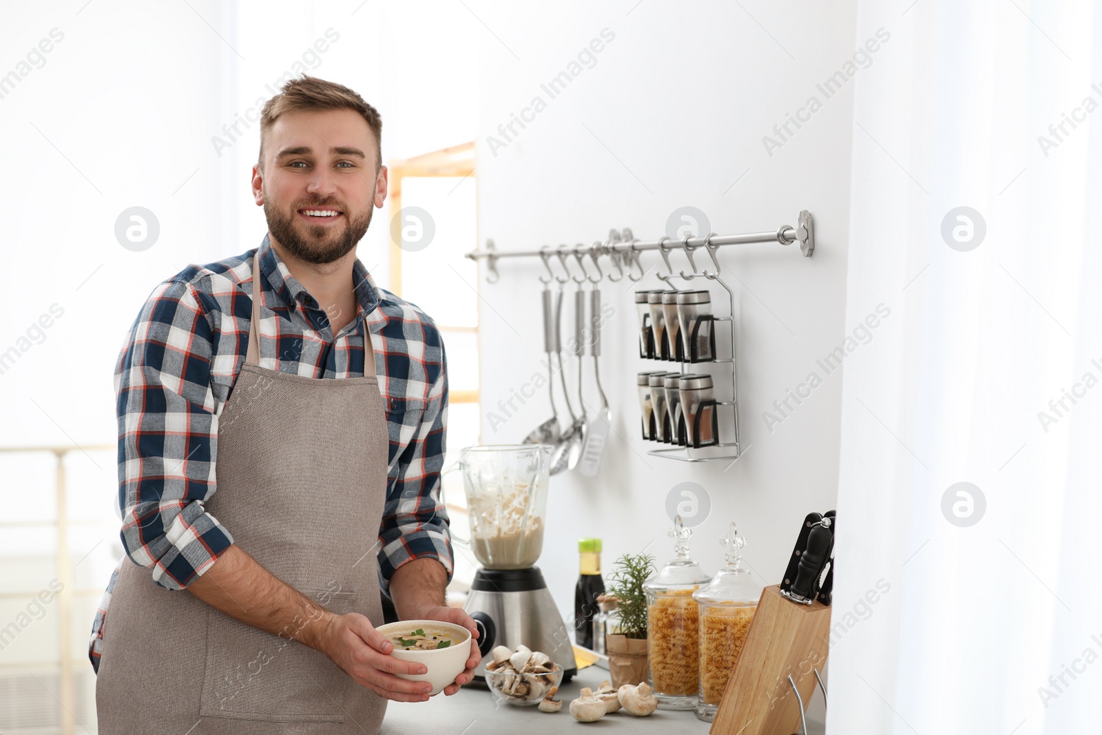 Photo of Young man holding bowl of tasty cream soup in kitchen