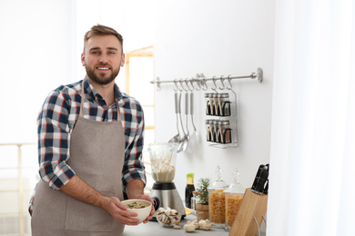 Photo of Young man holding bowl of tasty cream soup in kitchen