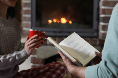 Couple reading book near burning fireplace at home, closeup