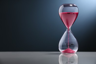 Photo of Hourglass with pink flowing sand on color background. Space for text