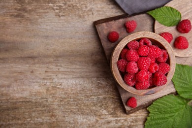 Photo of Bowl with fresh ripe raspberries and green leaves on wooden table, flat lay. Space for text