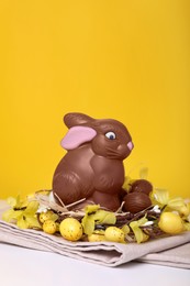 Photo of Beautiful composition with chocolate Easter bunny on white wooden table against yellow background