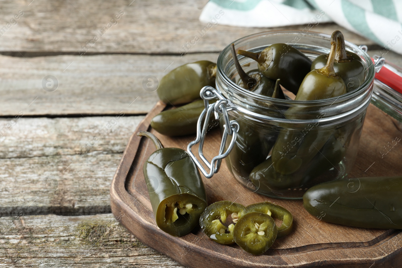 Photo of Pickled green jalapeno peppers on wooden table, space for text