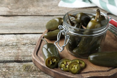 Photo of Pickled green jalapeno peppers on wooden table, space for text