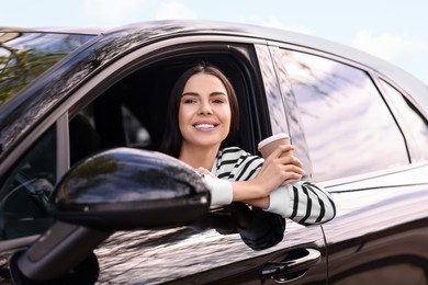 Photo of Young woman with cup of coffee sitting inside her modern car