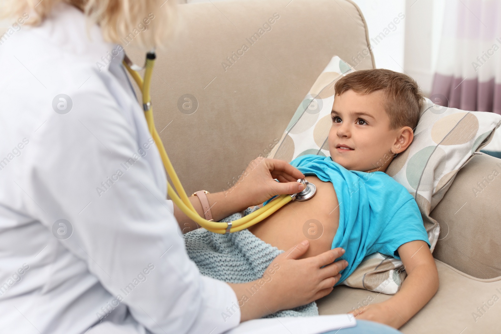 Photo of Children's doctor examining little boy with stethoscope at home