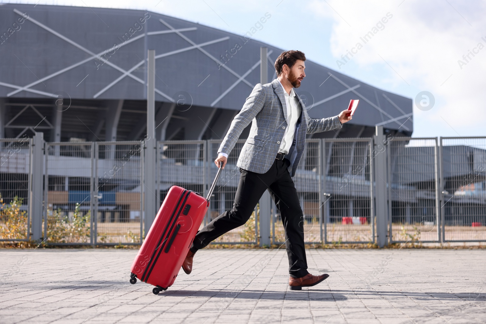 Photo of Being late. Businessman with red suitcase and passport running outdoors