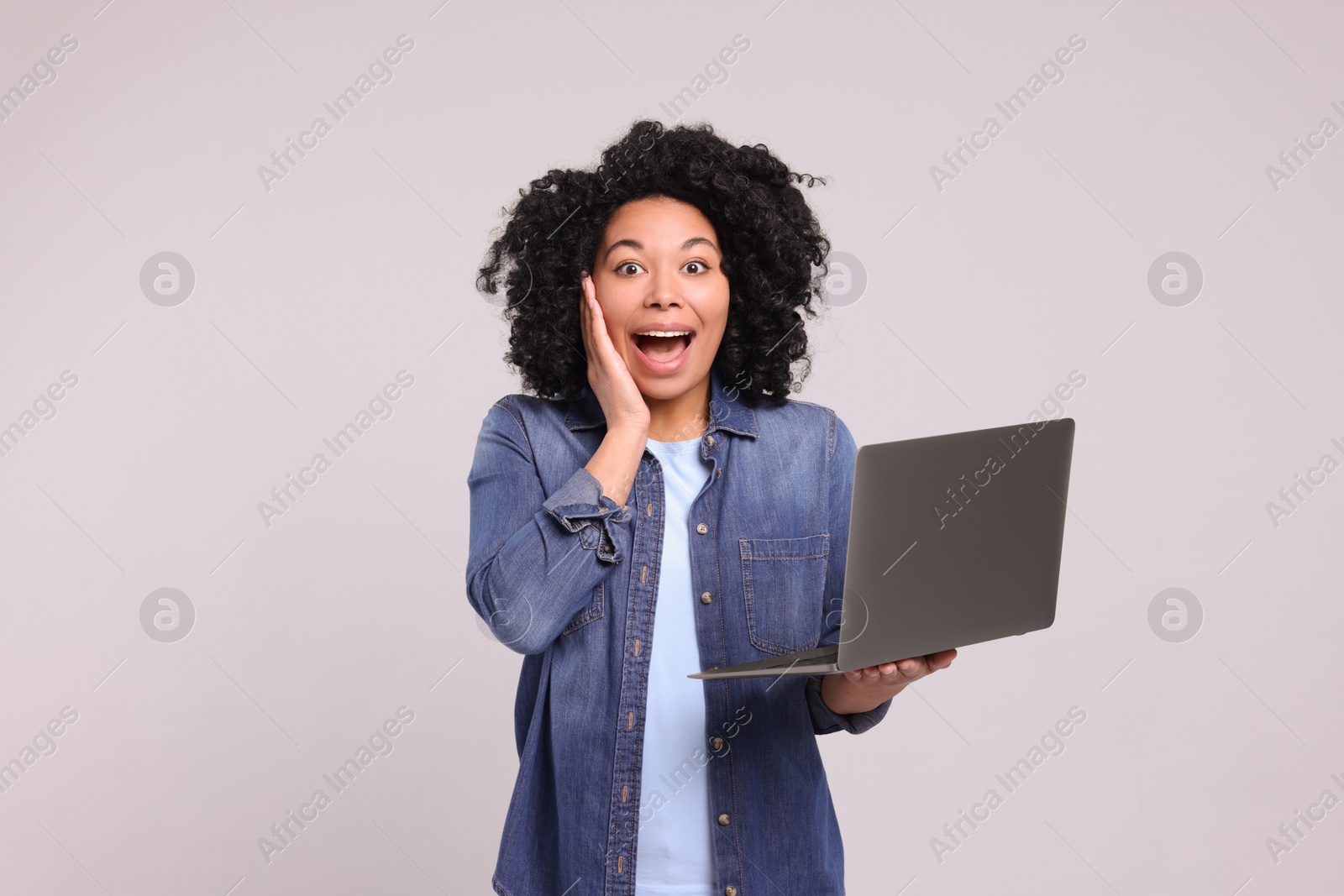 Photo of Emotional young woman with laptop on light grey background