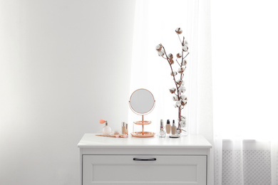 Photo of Small mirror and different makeup products on chest of drawers indoors