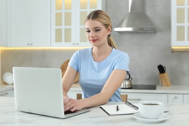 Photo of Home workplace. Woman typing on laptop at marble desk in kitchen