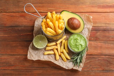 Photo of Parchment with french fries, guacamole dip, lime and avocado served on wooden table