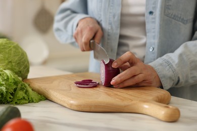 Woman cutting onion at white marble table in kitchen, closeup