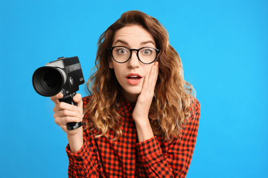 Beautiful young woman with vintage video camera on light blue background